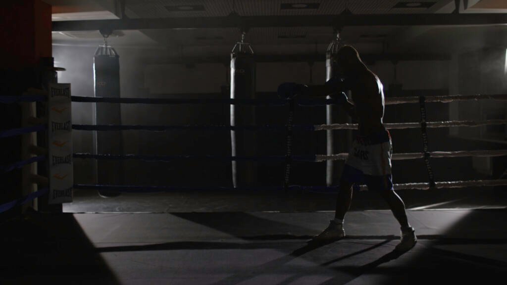 Un luchador de kickboxing practica boxeo de sombra en el ring. El atleta lucha contra su sombra. Un joven boxeador entrena lanzando un puñetazo con los puños vendados mientras se ejercita en el ring (4K). academia de boxeo en Calpe